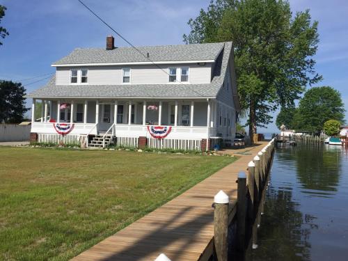 A white two-story house with patriotic decorations, surrounded by grass and a wooden dock along a calm waterway.