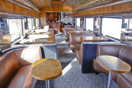 Interior of a vintage train car with brown leather seating and wooden tables, featuring large windows and a cozy atmosphere.