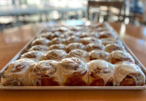 A tray of freshly baked cinnamon rolls topped with creamy icing, arranged neatly in a warm, inviting setting.