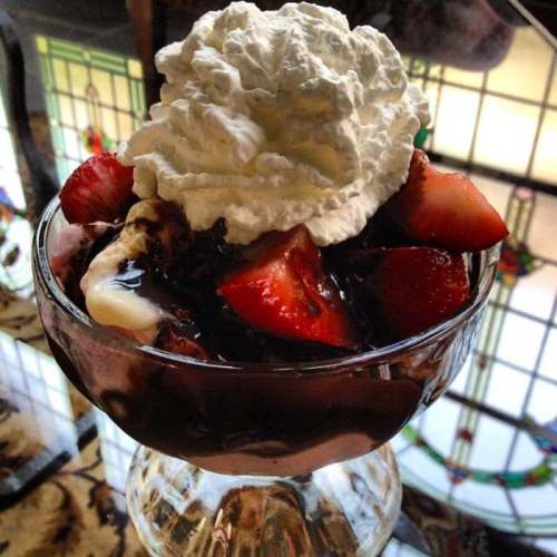 A glass dessert bowl filled with chocolate ice cream, fresh strawberries, and topped with whipped cream.