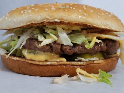 A close-up of a sesame seed bun burger filled with lettuce, pickles, and a juicy beef patty with melted cheese.