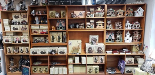 A wooden shelf filled with various decorative items, including figurines, model houses, and boxed collectibles.