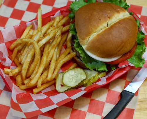 A burger with lettuce and tomato, served with crispy fries and pickles on a red and white checkered tray.