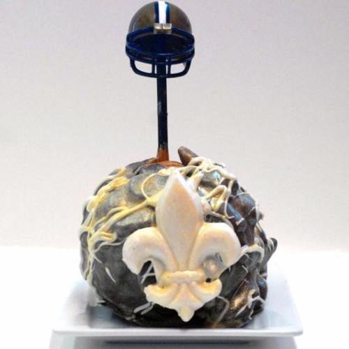 A decorative cake shaped like a football with a helmet on top and a fleur-de-lis design in white icing.