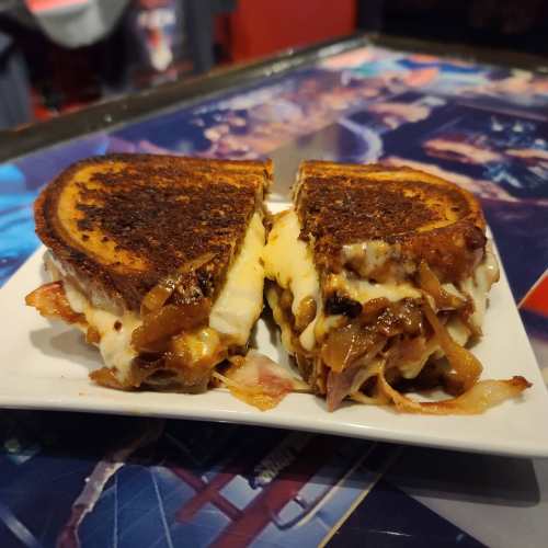 A grilled cheese sandwich with melted cheese and caramelized onions, cut in half on a white plate.