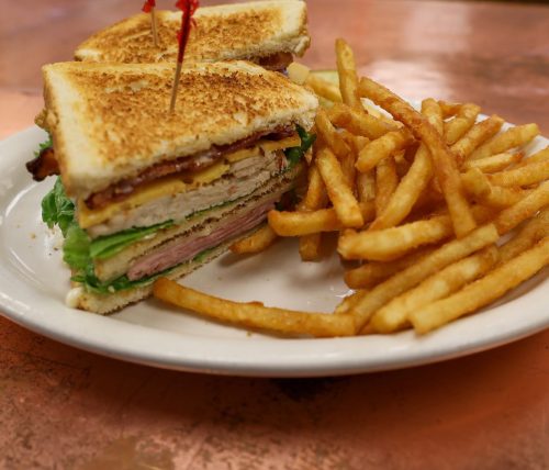 A toasted sandwich with layers of meat, cheese, and lettuce, served with a side of crispy French fries.