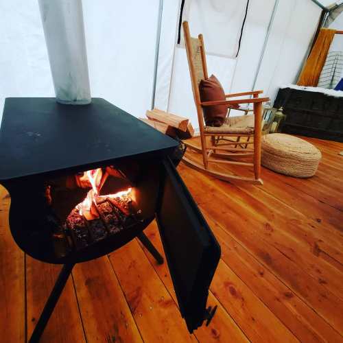 A cozy interior featuring a wood stove, a rocking chair, and a pouf on wooden flooring. Warm and inviting atmosphere.