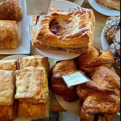 A variety of freshly baked pastries, including croissants, danishes, and puff pastries, displayed on white plates.