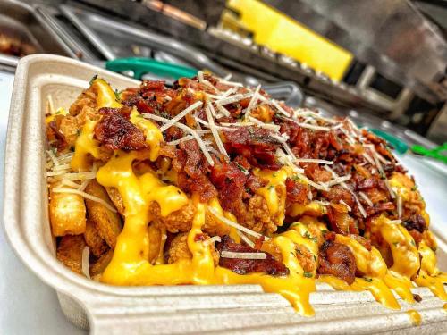 A close-up of loaded nachos topped with cheese, bacon, and grated Parmesan in a takeout container.