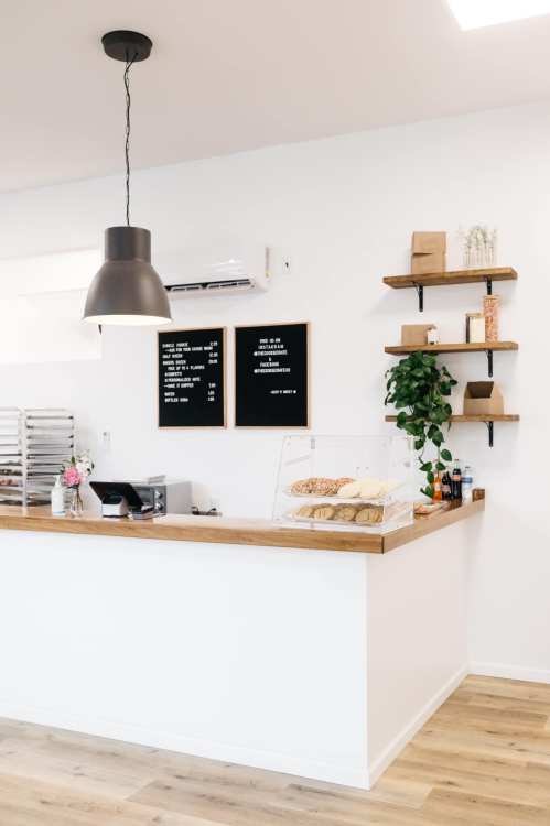 A modern cafe counter with a display of baked goods, menu boards, and decorative shelves with plants and items.