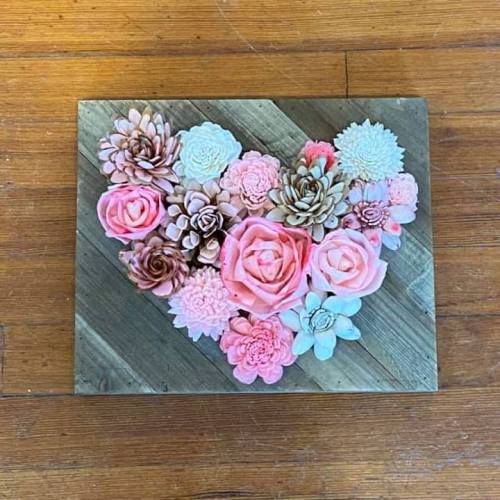 A heart-shaped arrangement of pink and cream flowers on a wooden background.