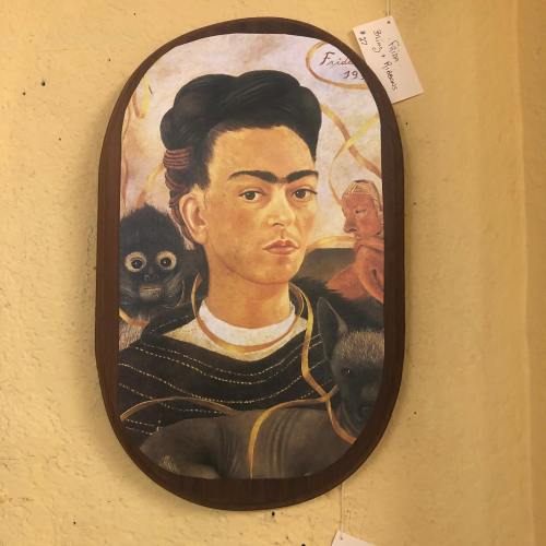 Frida Kahlo portrait featuring her with monkeys, set in an oval frame against a textured background.