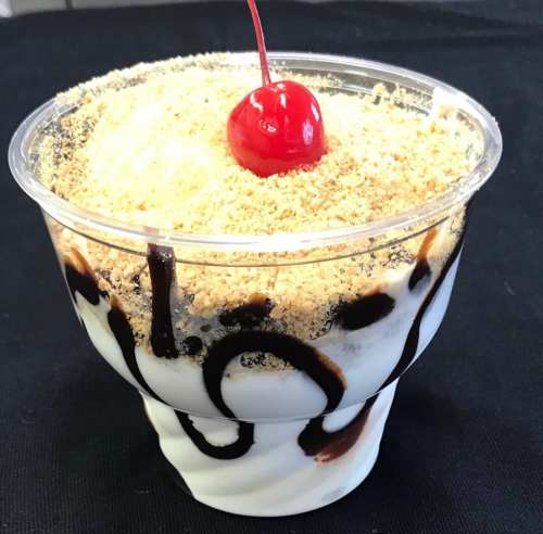 A dessert cup filled with layers of cream, topped with crushed cookies and a cherry.