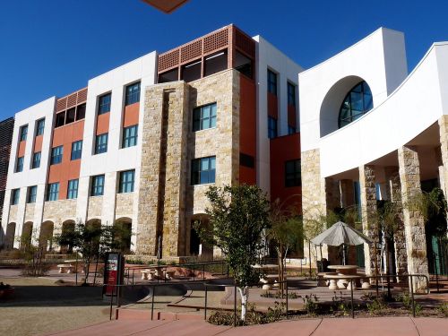 Modern building with stone accents, large windows, and a landscaped courtyard under a clear blue sky.