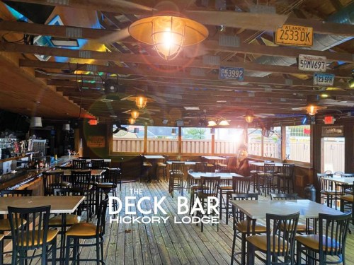 Interior of The Deck Bar at Hickory Lodge, featuring wooden floors, tables, and a bar with vintage license plates on the walls.