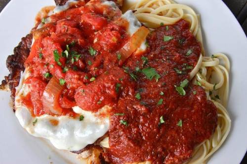 A plate of spaghetti topped with marinara sauce and a breaded chicken cutlet, garnished with parsley.