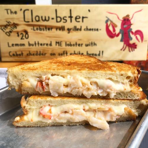 A grilled cheese sandwich filled with lobster, served on soft white bread, with a sign advertising the dish behind it.
