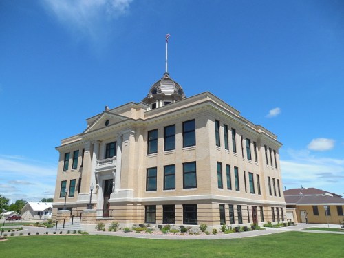 Historic brick building with a dome, large windows, and a flagpole, set against a blue sky and green lawn.