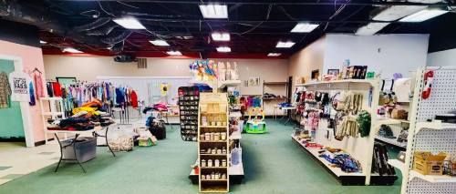 A thrift store interior with clothing racks, shelves of items, and a cluttered area of assorted goods.