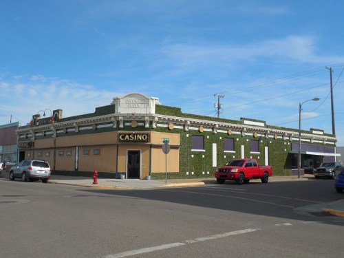 A green-covered casino building on a street corner, with parked cars and a clear blue sky in the background.