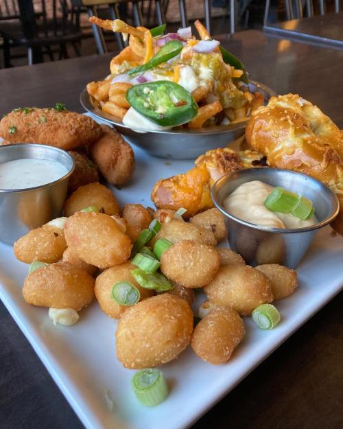 A platter of crispy snacks including cheese balls, fried pickles, and loaded fries topped with jalapeños and onions.