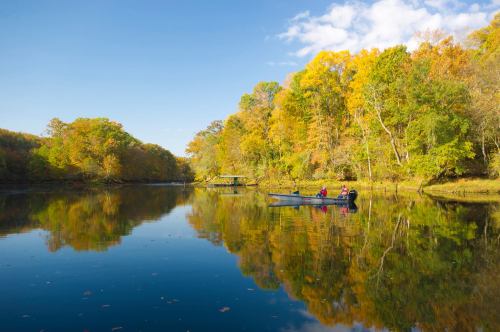 Two people in a canoe on a calm lake surrounded by vibrant autumn foliage and clear blue skies.