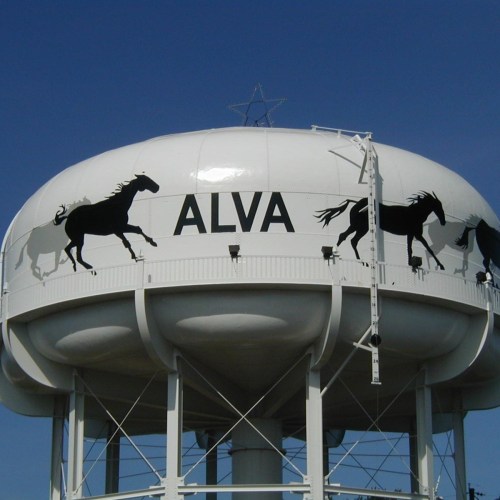 Water tower with the word "ALVA" and silhouettes of running horses against a clear blue sky.