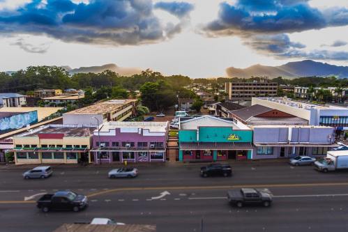 Aerial view of a colorful street with shops, cars, and mountains in the background under a cloudy sky at sunset.