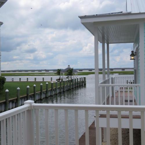 View of a calm waterway with a dock, green grass, and a cloudy sky, seen from a white balcony.