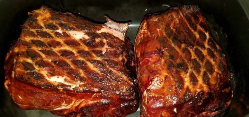 Two large, smoked meat roasts with a crispy, crosshatch pattern on the surface, resting in a dark cooking pan.