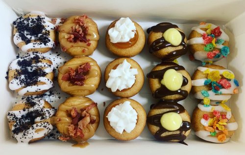 A box of assorted mini donuts topped with various flavors, including chocolate, caramel, and colorful cereal.