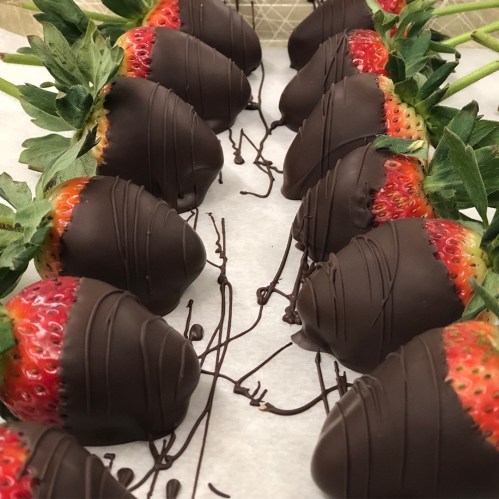 A row of chocolate-covered strawberries drizzled with dark chocolate on a white surface.