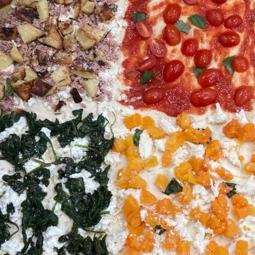 A colorful pizza with four sections: topped with apples, tomatoes, spinach, and butternut squash on a cheese base.