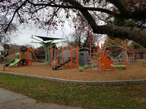 Colorful playground with slides, climbing structures, and swings, surrounded by trees and a grassy area.