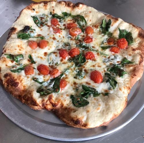 A freshly baked pizza topped with spinach and cherry tomatoes on a golden crust.