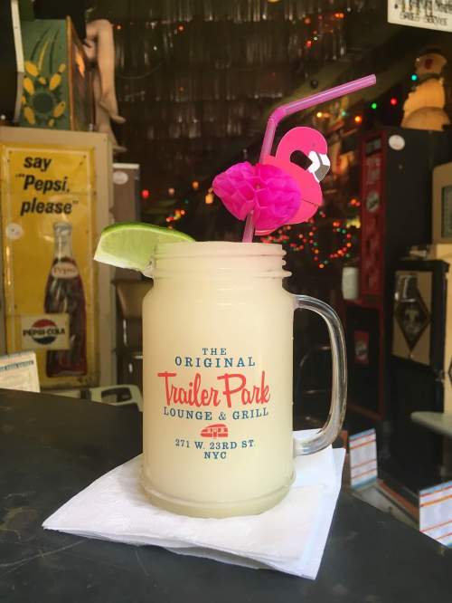 A refreshing drink in a mason jar with a lime wedge and a pink flamingo straw, set in a vibrant bar atmosphere.