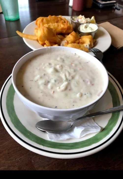 A bowl of creamy seafood chowder with a side of fried fish and dipping sauce on a plate.