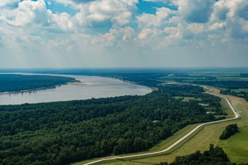Aerial view of a winding river surrounded by lush greenery and fields under a partly cloudy sky.