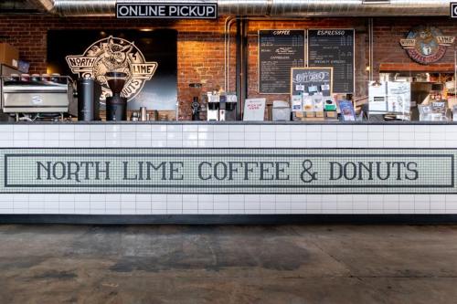 A coffee shop counter with a tiled sign reading "North Lime Coffee & Donuts" against a brick wall backdrop.