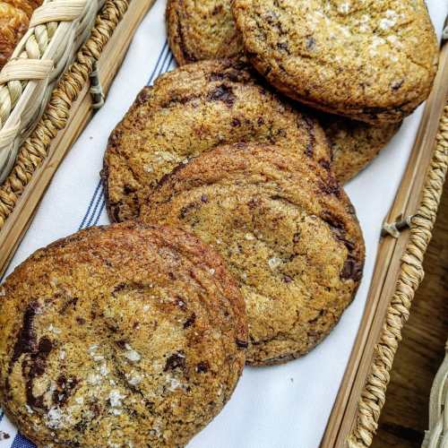 A close-up of freshly baked chocolate chip cookies arranged in a woven basket on a striped cloth.