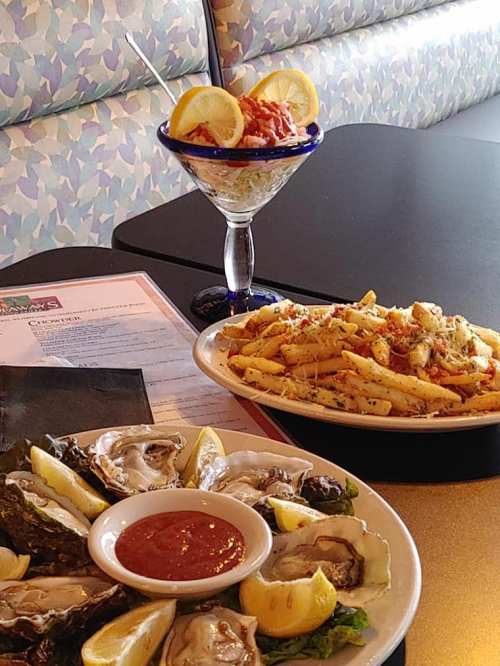 A plate of oysters with lemon and cocktail sauce, a pasta dish, and a dessert in a glass with lemon slices.