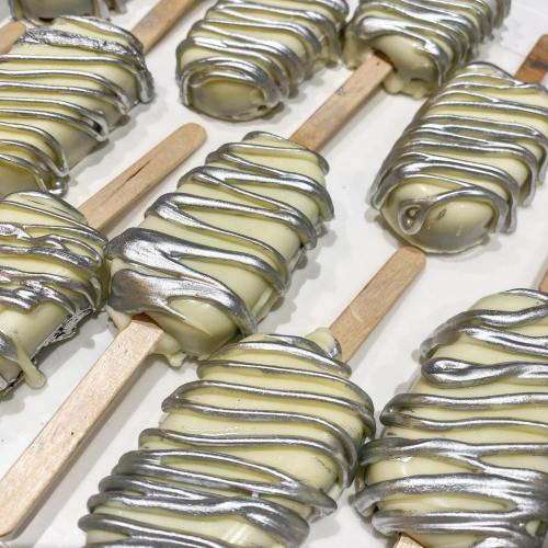 White chocolate-covered popsicles drizzled with silver icing on wooden sticks, arranged neatly on a tray.