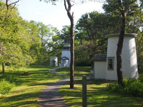 Two small lighthouses surrounded by trees on a grassy path, with a picnic area in the foreground.