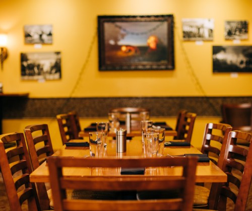 A cozy restaurant interior with wooden tables, chairs, and yellow walls adorned with framed photos.