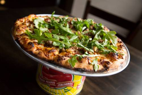 A freshly baked pizza topped with arugula and various ingredients, served on a colorful can.