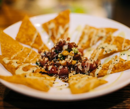 A plate of crispy nachos topped with a colorful mix of diced ingredients and drizzled with sauce.
