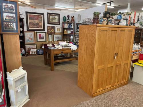 A cozy thrift store interior featuring wooden furniture, framed art, and various decorative items on display.