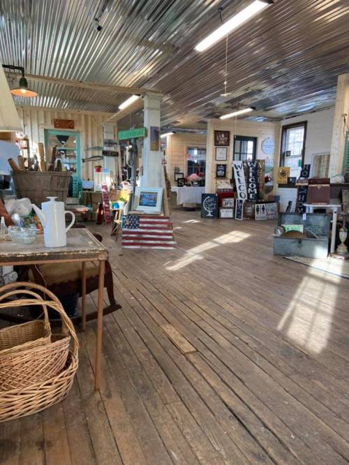 A rustic interior of a shop with wooden floors, various decor items, and an American flag display.