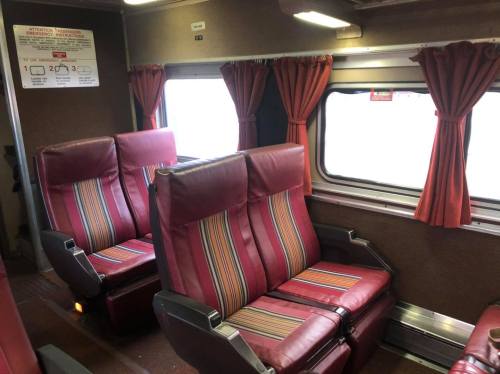 Interior of a train carriage featuring red and striped seats with curtains at the windows.