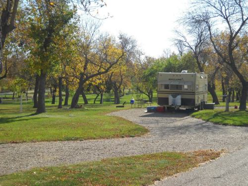 A vintage RV parked in a grassy area surrounded by trees with autumn leaves, near a gravel path.